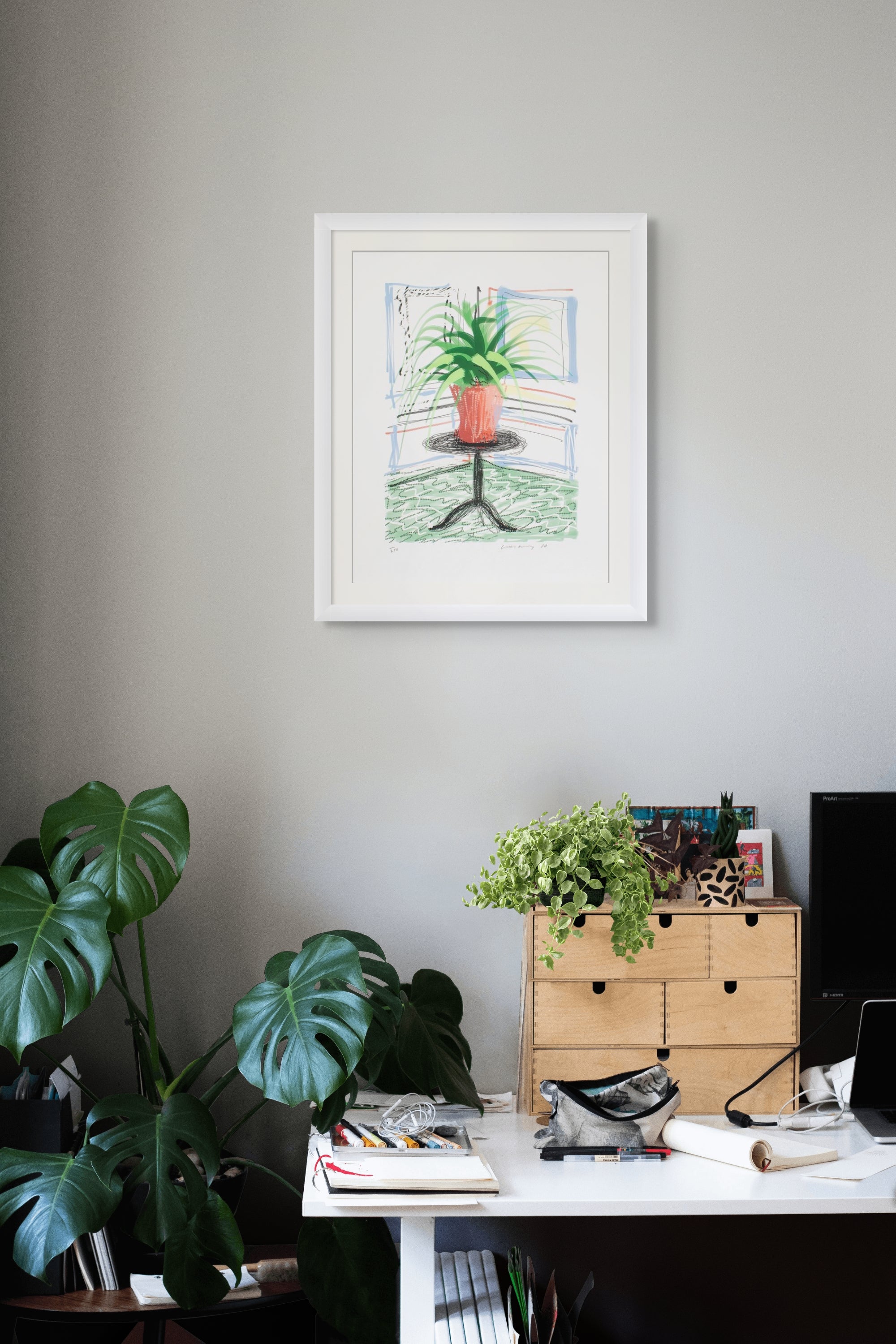 Home office with a desk, plants, and framed david hockney ipad drawing artwork on a wall.
