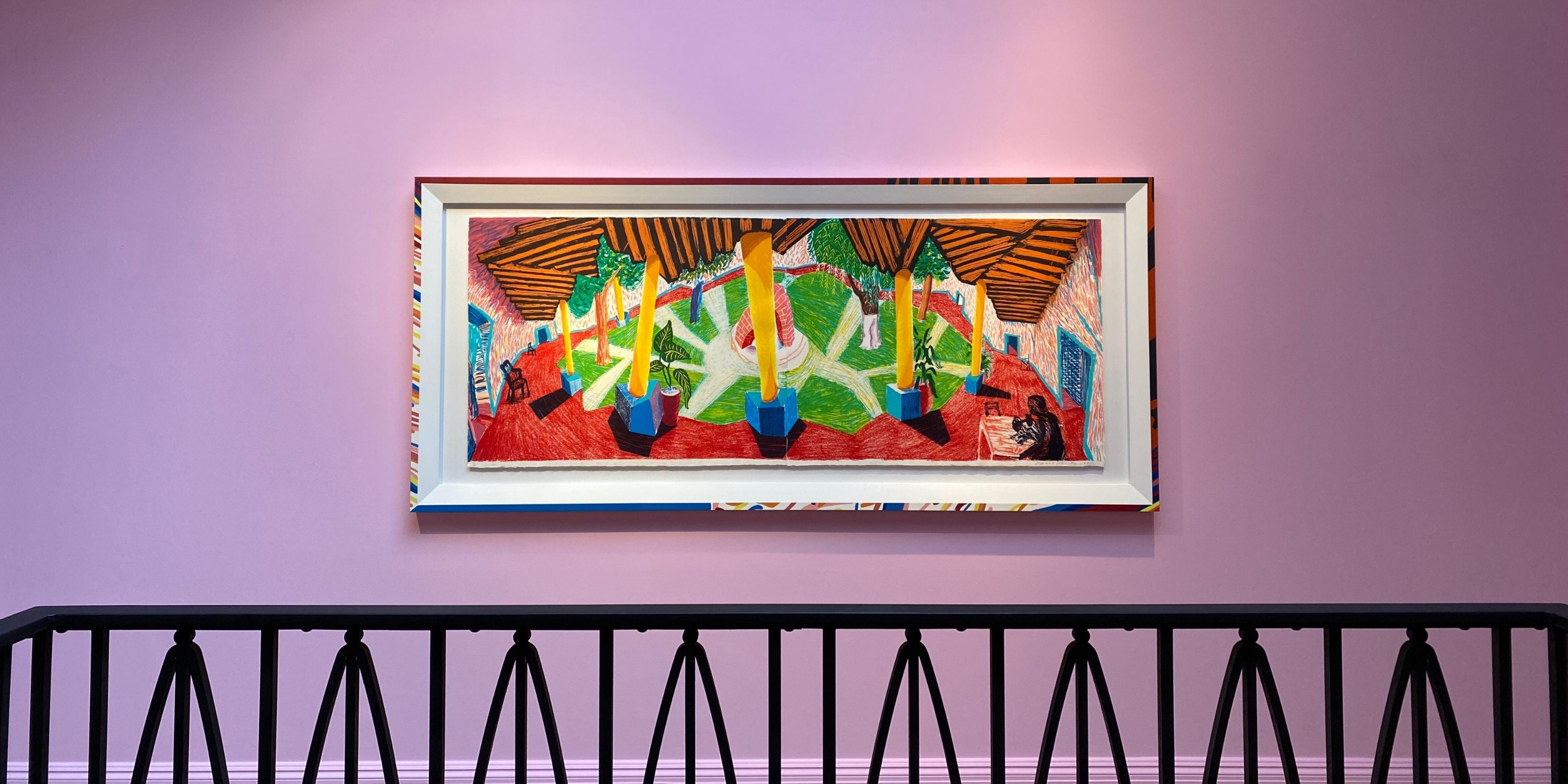 Colourful abstract painting by David Hockney exhibition at art gallery in London on a pink wall with a black metal railing below.