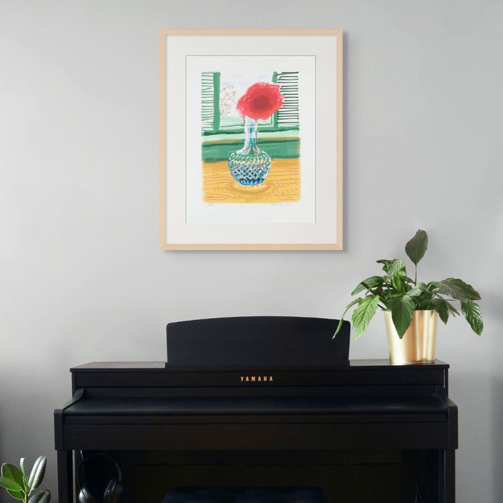 Framed David Hockney iPad Drawing artwork of a red flower in a glass vase on a gray wall above a Yamaha piano.
