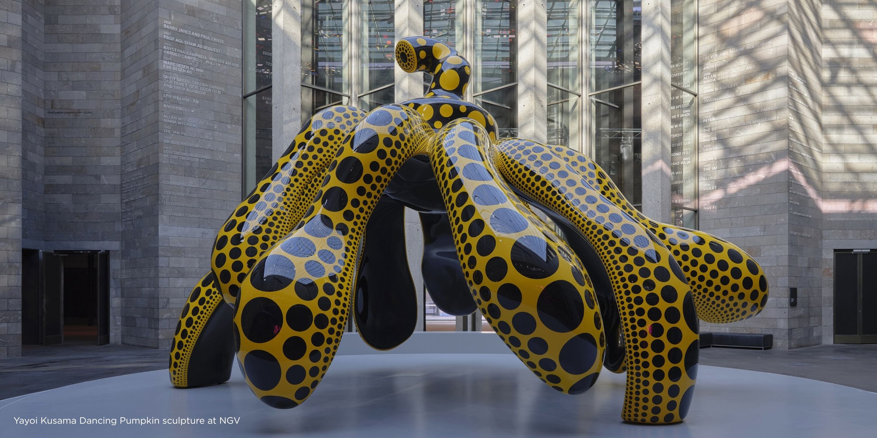 Yellow and black polka dot sculpture resembling a dancing pumpkin in an indoor setting. Yayoi Kusama Dancing Pumpkin sculpture at NGV