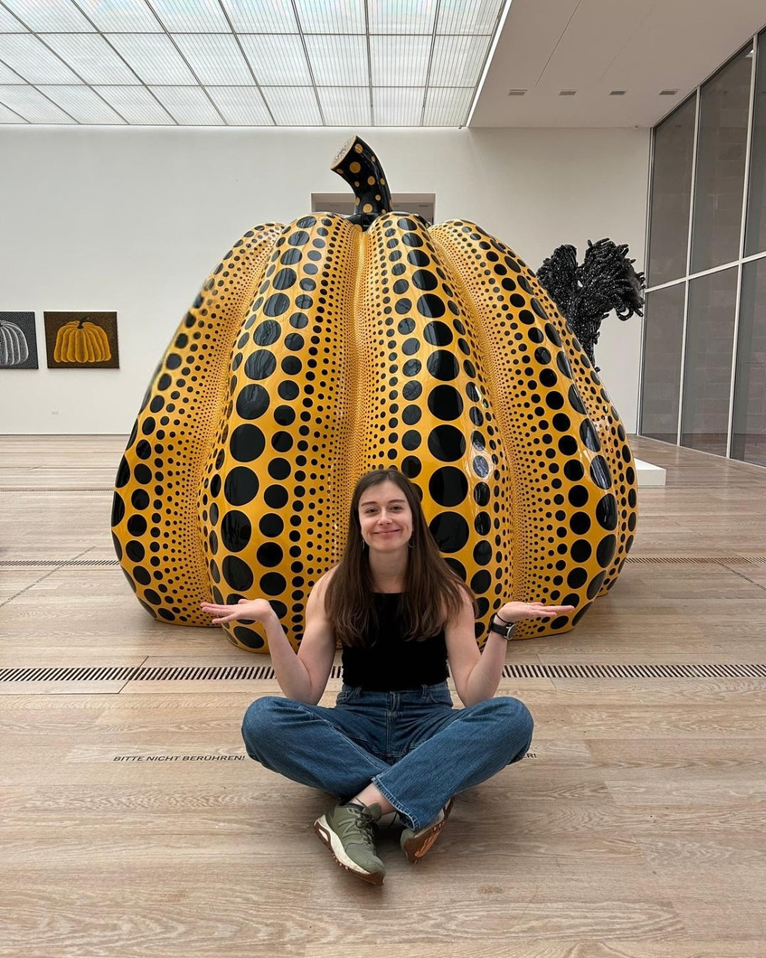 Woman sitting in front of a large, patterned pumpkin sculpture in an indoor setting.