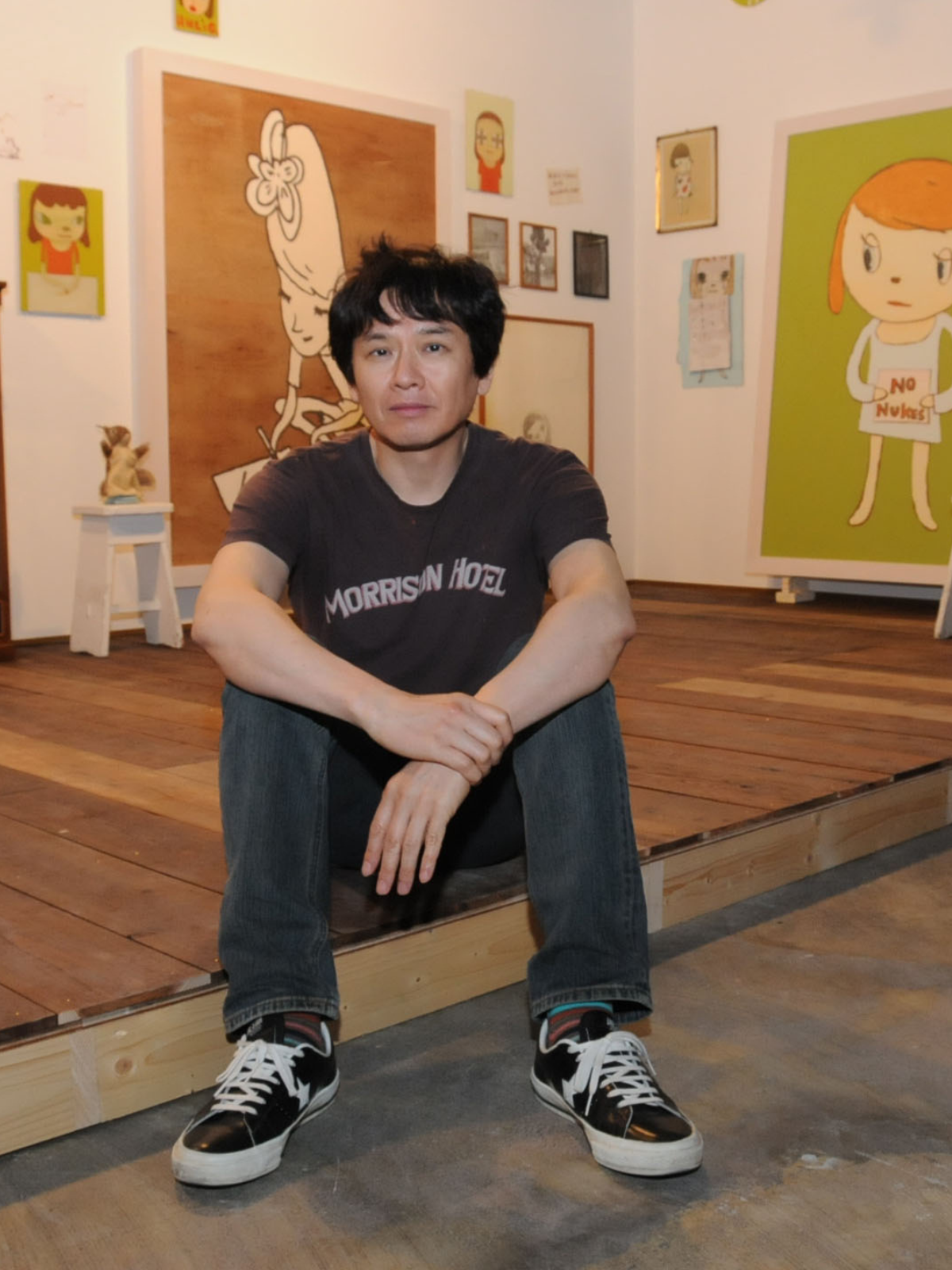 Yoshitomo Nara Japanese artist sitting in his studio with paintings